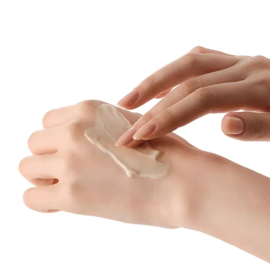 A close-up of a hand applying a smooth, creamy beige cosmetic cream to the back of another hand against a solid white background.