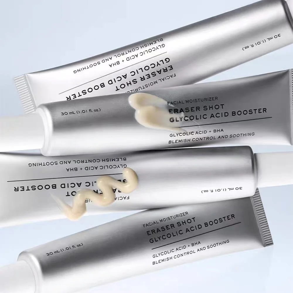 Four silver squeeze tubes of facial moisturizer arranged diagonally on a light blue background, with a dollop of pale cream product resting on one tube. The text on the tubes reads 'ERASER SHOT GLYCOLIC ACID BOOSTER' and 'FACIAL MOISTURIZER'.