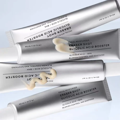 Four silver squeeze tubes of facial moisturizer arranged diagonally on a light blue background, with a dollop of pale cream product resting on one tube. The text on the tubes reads 'ERASER SHOT GLYCOLIC ACID BOOSTER' and 'FACIAL MOISTURIZER'.