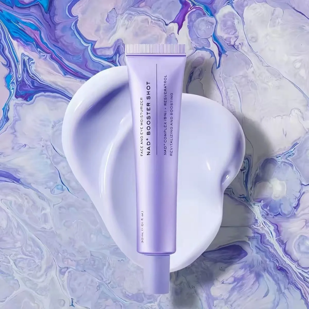 A lavender purple tube of face moisturizer labeled 'NAD+ BOOSTER SHOT' is centered on a glossy white abstract shape against a marbled purple, blue, and white background.