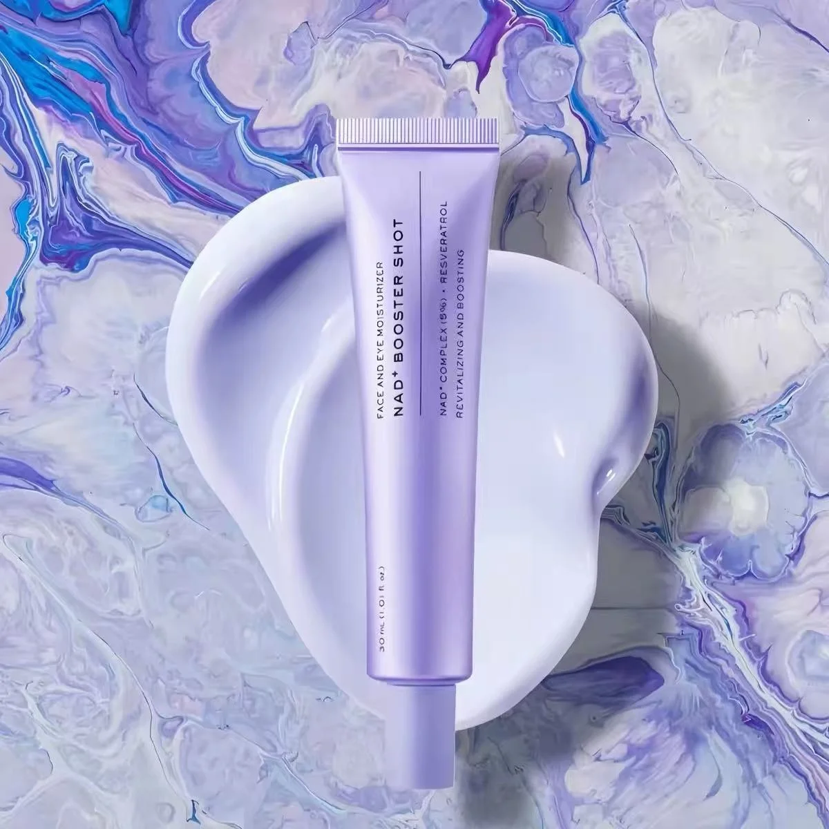 A lavender purple tube of face moisturizer labeled 'NAD+ BOOSTER SHOT' is centered on a glossy white abstract shape against a marbled purple, blue, and white background.