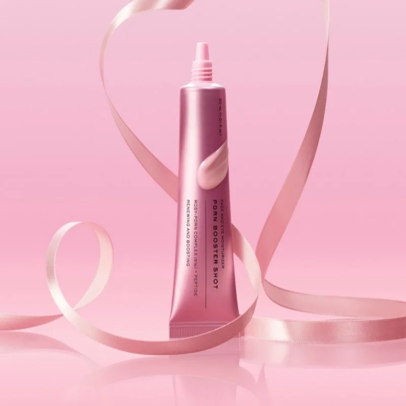A pink squeeze tube of FOrm Boostershot retinol serum, styled with a flowing pink ribbon on a solid pink background.