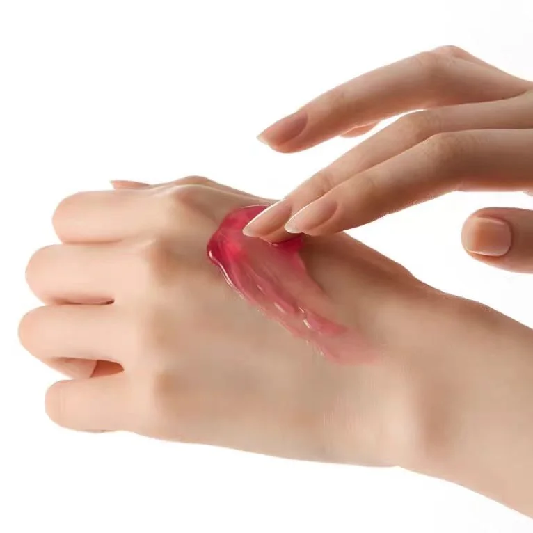 A close-up of a hand applying a translucent pinkish-red cosmetic gel or cream with a finger, set against a clean white background.